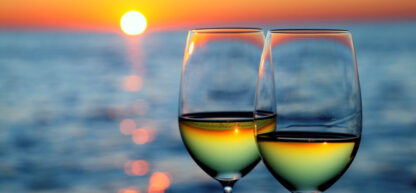 Two glasses of wine with a view of a sunset by the ocean.